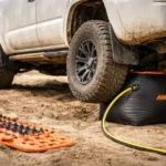 Airbag jack lifting an SUV on sand during off-road recovery with traction boards nearby